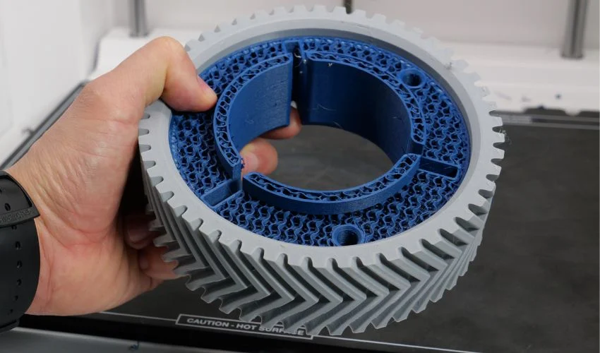 Többanyagú filamentes 3D nyomtatással készült fogaskerék szürke külső testtel és kék belső szerkezettel